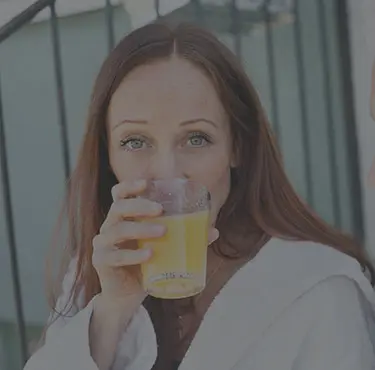 Två personer sitter utomhus och en av dem dricker ett glas juice