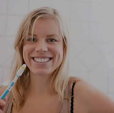 Person håller i tandborste och ler stort
