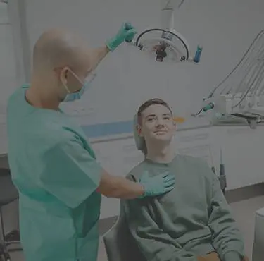 Patient ligger i en tandläkarstol och tittar på tandläkare med munskydd.