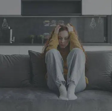 Kvinna sitter i soffa och sliter sitt hår.