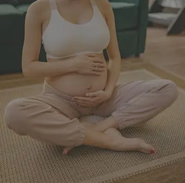 En person sitter i skräddarställning på golvet och håller om sin gravida mage.