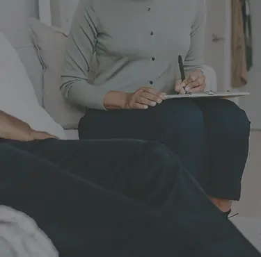 En kvinnlig psykolog sitter bredvid sin patient i en soffa och antecknar i ett block.