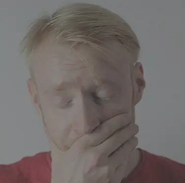 En man blundar och håller sin ena hand för munnen.