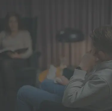Psykoterapeut sitter mittemot en patient som lutar huvudet mot sin hand.