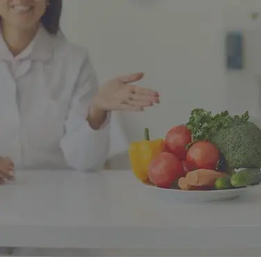 En vitklädd person som pekar med hela handen mot ett fat med grönsaker