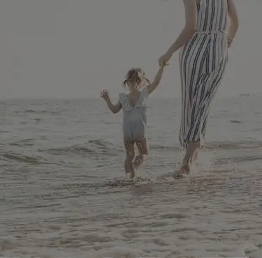 Kvinna och barn i strandkläder med badklåda som håller hand och är på väg ut i vattnet.