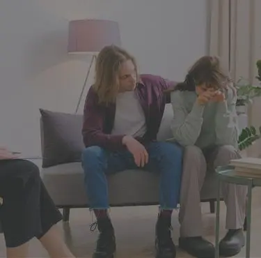 Två personer sitter på en soffa, och den ena tröstar den andra.