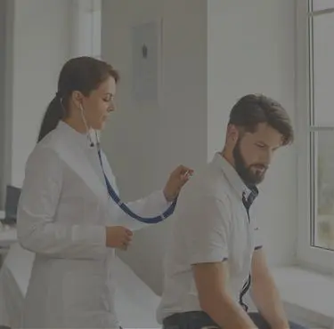 En läkare lyssnar på en patients lungor med ett stetoskop.