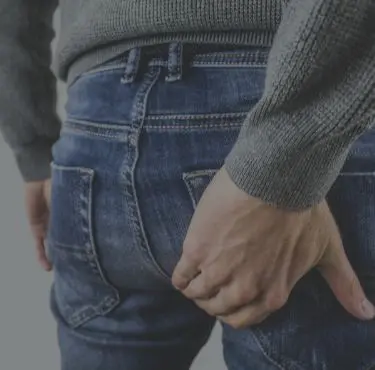 Man i jeans har hemorrojder och håller i rumpan