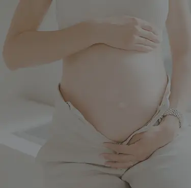 En gravid kvinna med uppknäppta byxor håller om sin mage.