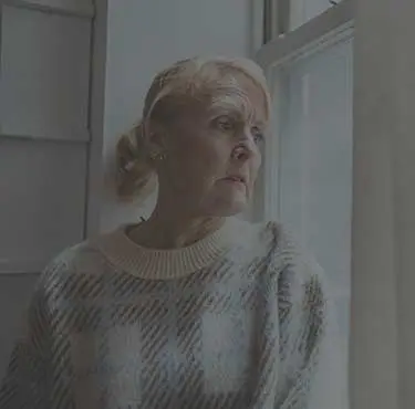En äldre kvinna tittar ut genom ett fönster