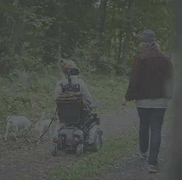 En kvinna i elrullstol på promenad i sällskap med en man och två hundar