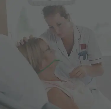 Kvinna ligger i sjukhussäng och får hjälp med andningen.