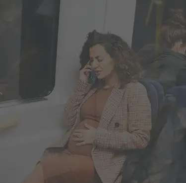 Gravid kvinna på tunnelbanan pratar i telefon och ser besvärad ut med handen över magen.