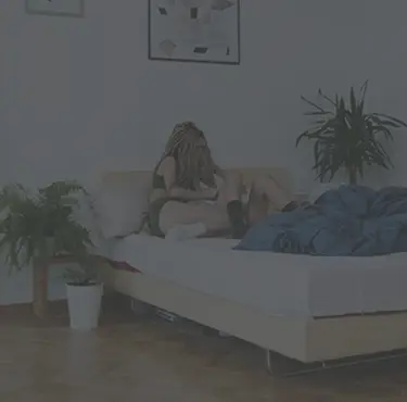 Två kvinnor sitter i en säng i underkläder, och den ena håller om den andra.