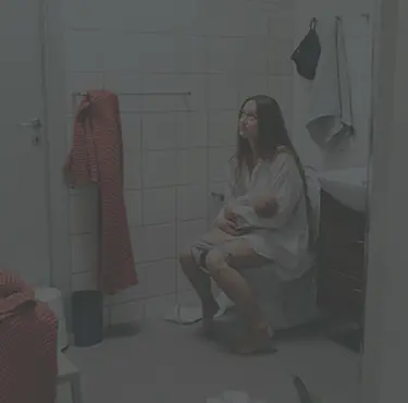 Kvinna sitter på toaletten med ett spädbarn i famnen