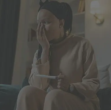 En person sitter på en soffa med ett graviditetstest i handen och håller handen för ansiktet.