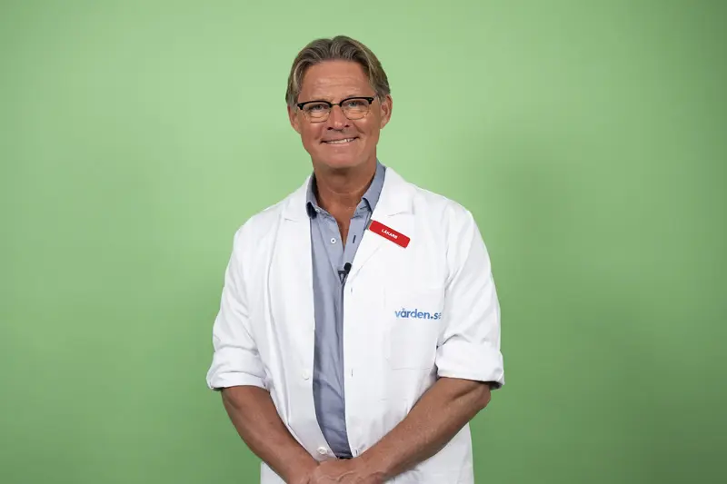 Doktor Mikael Sandström ler stort med läkarrock mot en grön bakgrund