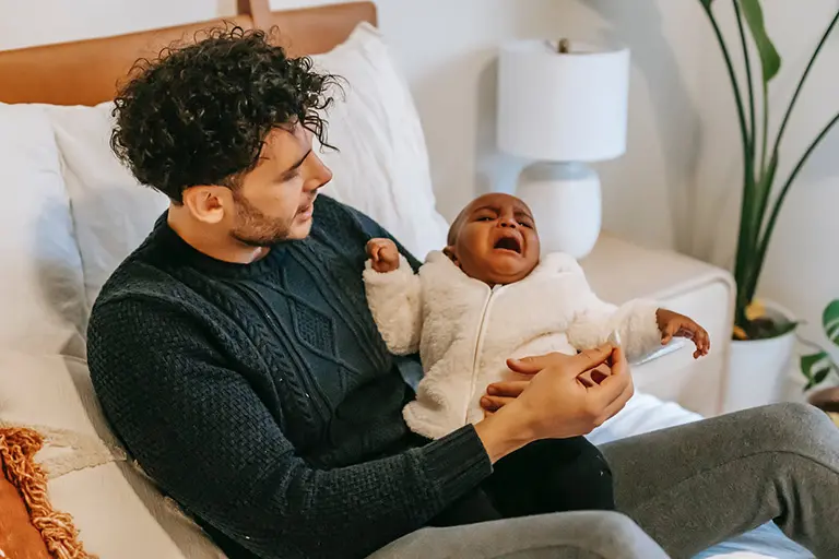 Person sitter i en säng och håller i en skrikande bebis