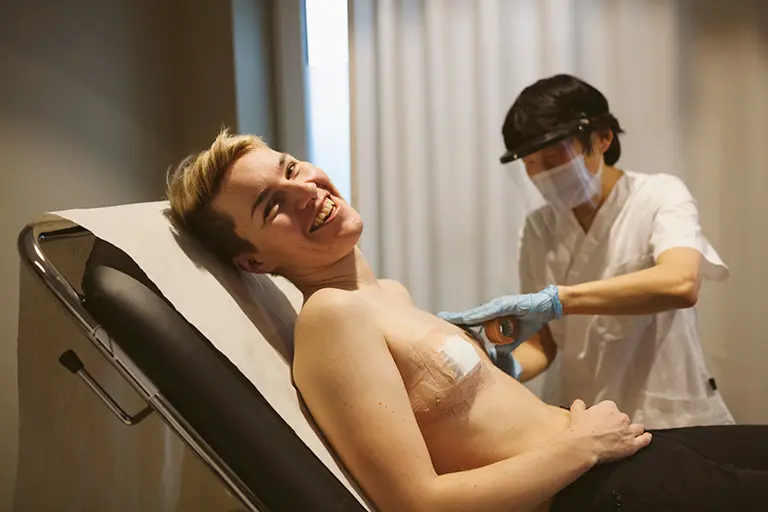 En leende patient får hjälp av sjuksköterska att ta bort förband från bröstkorgen efter kirurgi.