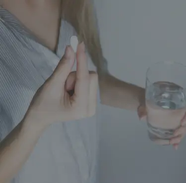 En person som håller i en tablett och ett glas vatten.