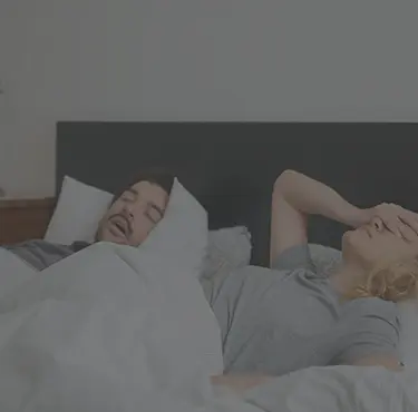 Kvinna irriterad på partner med sömnapné som snarkar i sängen och vill att han gör en sömnapnéutredning